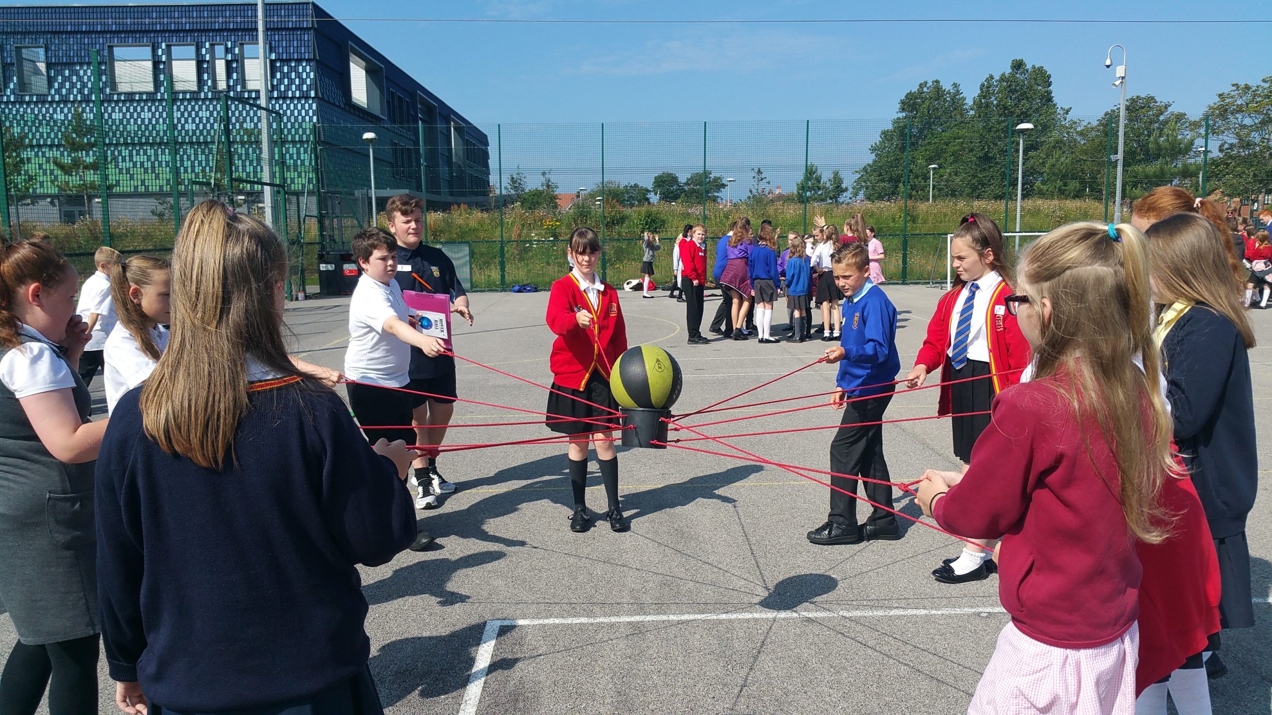 Young children in school uniforms holding ropes for a team building activity